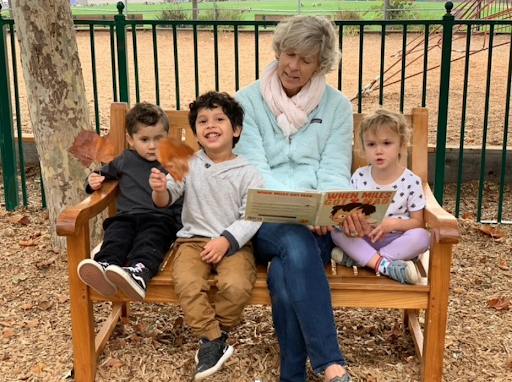 Founder Carol Thomsen reading a book to three pre-schoolers sitting on a bench